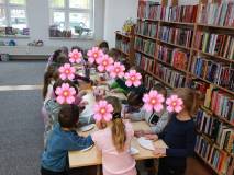 Dzieci stoją przy stolikach i wykonują pracę plastyczną