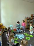 Dzieci siedzą na dywanie, a bibliotekarka pokazuje dzieciom obrazki 