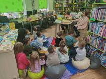 Bibliotekarka skryta za teatrzykiem kamishibai czyta dzieciom „Trzy świnki”