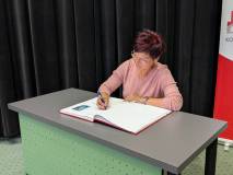 Wpis do księgi pamiątkowej
Zdjęcie przedstawia kobietę z krótkimi, ciemnoczerwonymi włosami i w oku