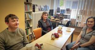 Uczestnicy spotkania, siedzący przy stoliku w czytelni Biblioteki. na stole cukierki, owoce i filiża