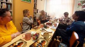 Uczestniczki spotkania siedzą w czytelni biblioteki, rozmawiają. Na stole leżą omawiane książki, kub