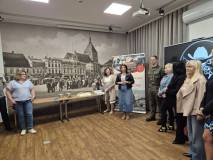 Zdjęcie przedstawia oficjalne spotkanie grupy osób w sali konferencyjnej. Pośrodku stoi długi stół, 