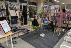 Szerszy widok spotkania autorskiego w bibliotece. Dwie osoby siedzą na zielonych fotelach, a stojąca