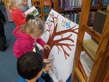 Dzieci naklejają pokolorowane ilustracje zwierząt na namalowane na brystolu drzewo