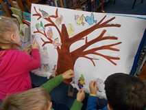 Dzieci ozdabiają namalowane na brystolu drzewo