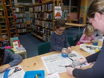 Bibliotekarka wspomaga dzieci w wykonywaniu pracy plastycznej