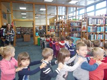 Dzieci ustawione za bibliotekarką poruszają się w rytm muzyki