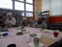 Panie siedzą przy stole i pokazują przyniesione przez siebie włóczki