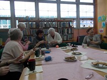 Panie siedzą przy stole i pokazują sobie swoje rękodzieła