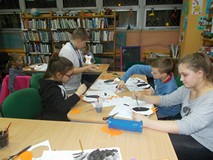 Dzieci siedzą przy stole i malują pingwiny