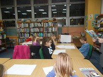 Dzieci siedzą przy stole i słuchają bibliotekarki, która czyta książkę o pingwinie