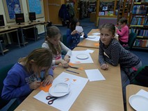 Dzieci siedzą przy stole i wycinają elementy pracy plastycznej