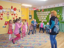 Bibliotekarka stoi przed dziećmi, które skaczą w rytm muzyki