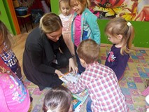 Bibliotekarka trzyma książki, a dzieci stoją wokół niej