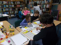 dzieci siedzą przy stołach i malują farbami