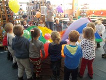 Bibliotekarka wraz z dziećmi podrzuca balony na chuście animacyjnej