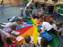 Dzieci kolorują ilustracje na chuście, a bibliotekarka wspomaga ich pracę