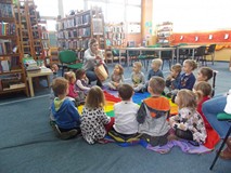 Dzieci siedzą na chuście i patrzą w kierunku prowadzącej, która trzyma w rękach koszyczek