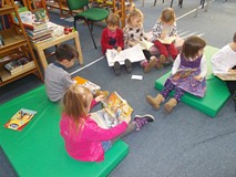 Dzieci siedzą na materacach i oglądają książki