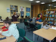 Biblioterka stoi przed dziećmi, które siedzą przy stołąch i trzyma w ręku czasomierz