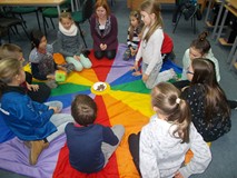 Dzieci siedzą na chuście animacyjnej i rzucają pluszową kostką