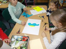 Dzieci siedzą przy stole i wykonują prace plastyczną w drużynie