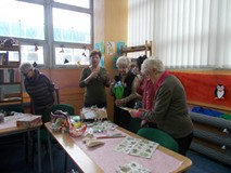 Panie stoją przy stole i pokazują sobie swoje rękodzieła