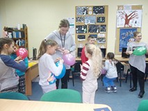 dzieci stoją z balonami, a bibliotekarka pomaga zawiązać balona