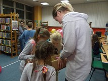 dzieci wybierają upominki z kartonu trzymanego przez bibliotekarkę