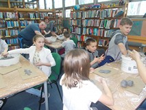 Dzieci siedzą przy stołach, a bibliotekarka i gość pomagają w tworzeniu rzeźb