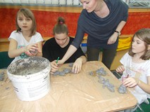 Dzieci siedzą przy stole, a bibliotekarka obserwuje ich pracę