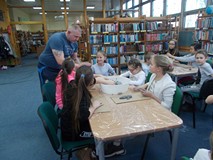 Dzieci siedzą przy stole, a nasz gość pomaga im w rzeźbieniu pięknych figur z masy papierowej