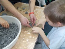 Dzieco siedzi i rzeźbi krokodyla, a gość koordynuje jego pracę