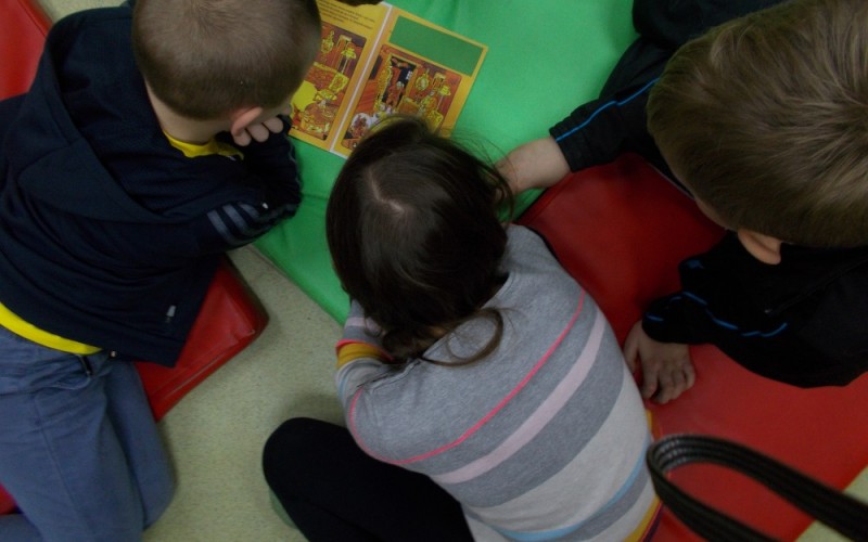 Kilkoro dzieci siedzi na kolorowych materacach i rozwiązuje kolorowe zagadki z ksiązki...