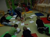 Grupa dzieci leży na materacach, rozlożonych w koło i wszyscy skierowani są do środka. Przed każdym 