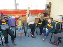 Dzieci siedzą na krzesłach i czytają z kartki