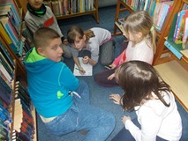 Dzieci siedzą razem w grupie na dywanie i piszą wspólne odpowiedzi