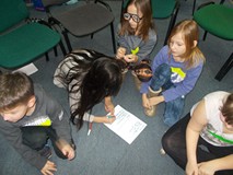 Dzieci siedzą w grupie i piszą swoje wyniki prac