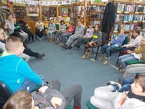 Dzieci z bibliotekarkami siedzą na krzesłach w kole