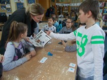 Bibliotekarka pokazuje książkę dzieciom siedzącym przy stole
