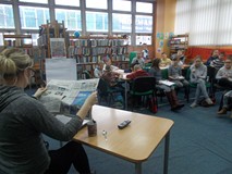 Bibliotekarka przebrana za detektywa siedzi przed grupą i czyta gazetę