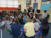 Bibliotekarka siedzi z dziećmi na chuście animacyjnej i czyta list