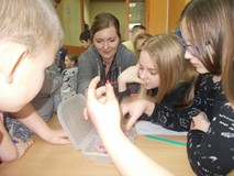 Dzieci z bibliotekarką siedzą i oglądają figurki z modeliny