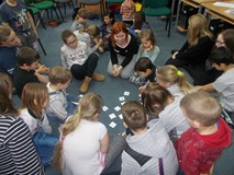 dzieci z bibliotekarką siedzą na dywanie w kole i losują kartki