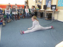 Dziewczynka robi szpagat przed dziećmi siedzącymi na widowni