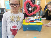 Dziewczynka stoi przed figurką z klocków i trzyma w ręku balon w kształcie serca