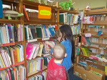 Troje dzieci stoją przed regałem i szukają książek