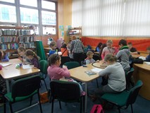 Dzieci siedzą przy stole a bibliotekarka pomaga dzieciom w pracy