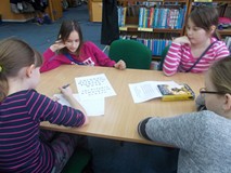 Dzieci siedzą przy stole i w drużynie zapisują odpowiedzi